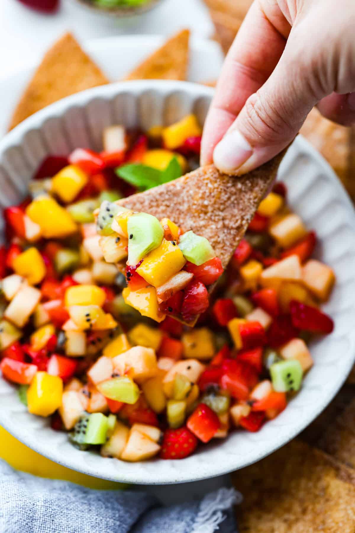 Someone taking a scoop of fruit salsa with a cinnamon sugar chip. 