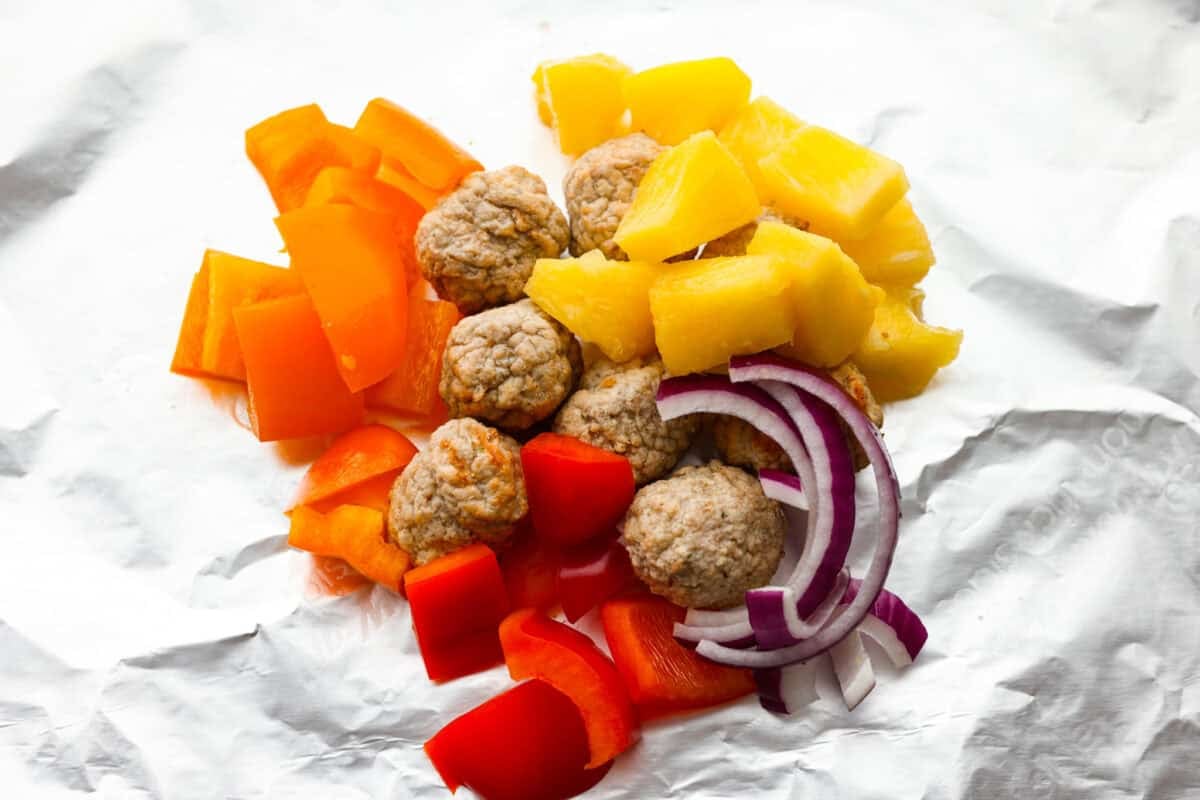 These meatball foil packets have juicy meatballs, sweet pineapple, colorful veggies, covered in sticky teriyaki sauce, and grilled to perfection. Easy to make, fun to eat, and no dishes to wash! Yes, please! Veggies, pineapple, and meatballs in the middle of the piece of foil.