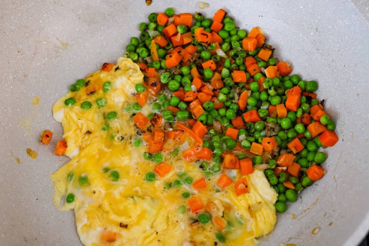 Eggs being cooked next to the veggies in a skillet.