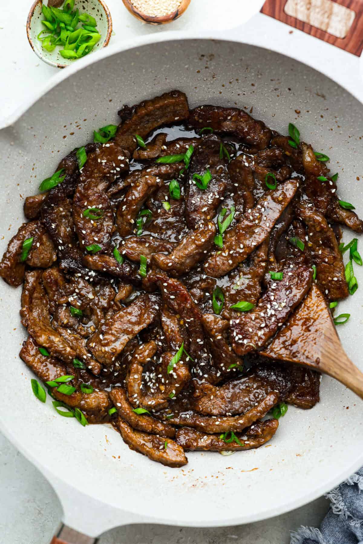 Skillet with beef teriyaki garnished with sesame seeds and green onion. 