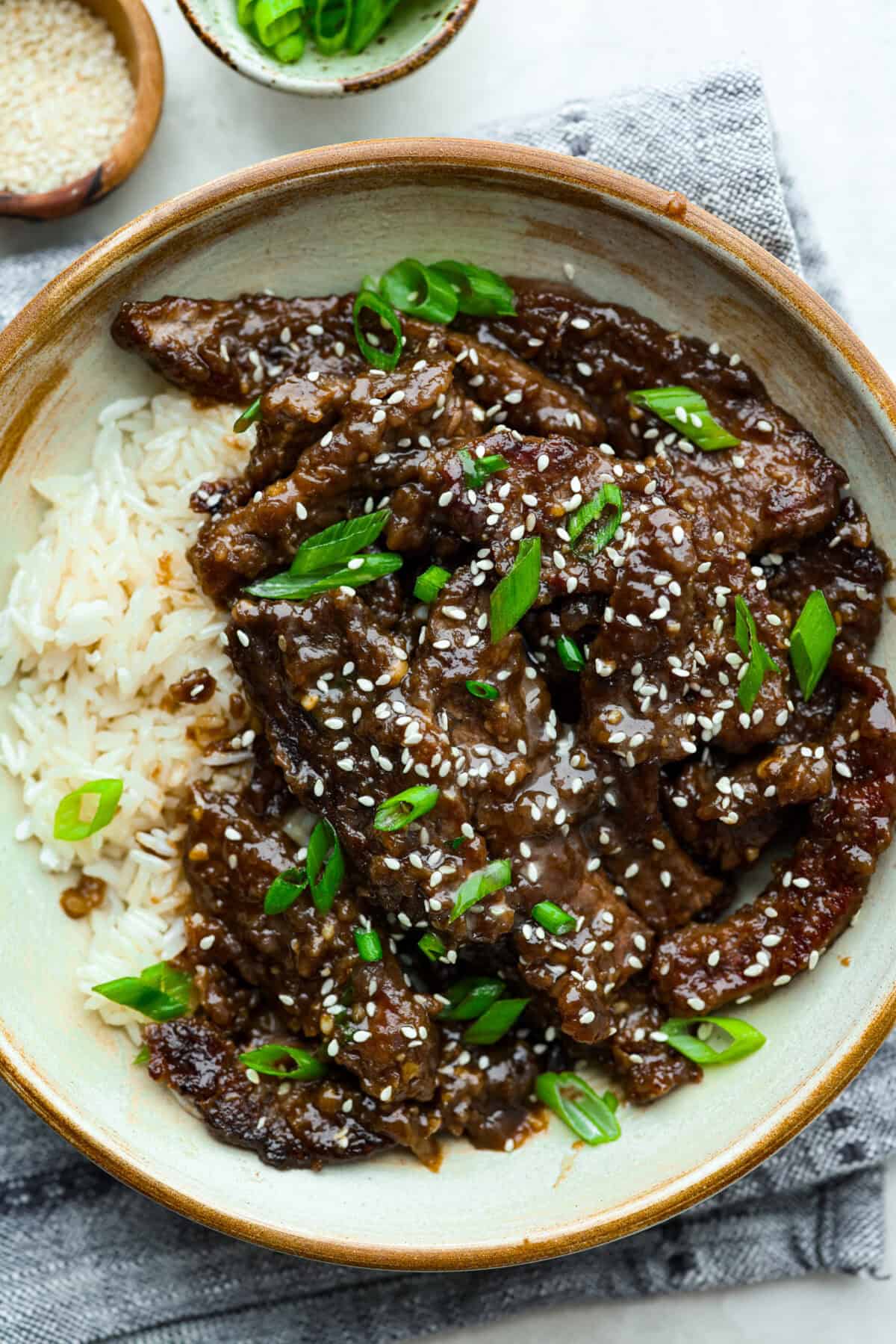 My family is obsessed with my better-than-takeout Beef Teriyaki. The secret? Velveting the beef! Itโs simple, but it makes it unbelievably tender. Trust me, youโll want this trick in your back pocket. Bowl of garnished beef teriyaki with white rice, sesame seeds and green onions.