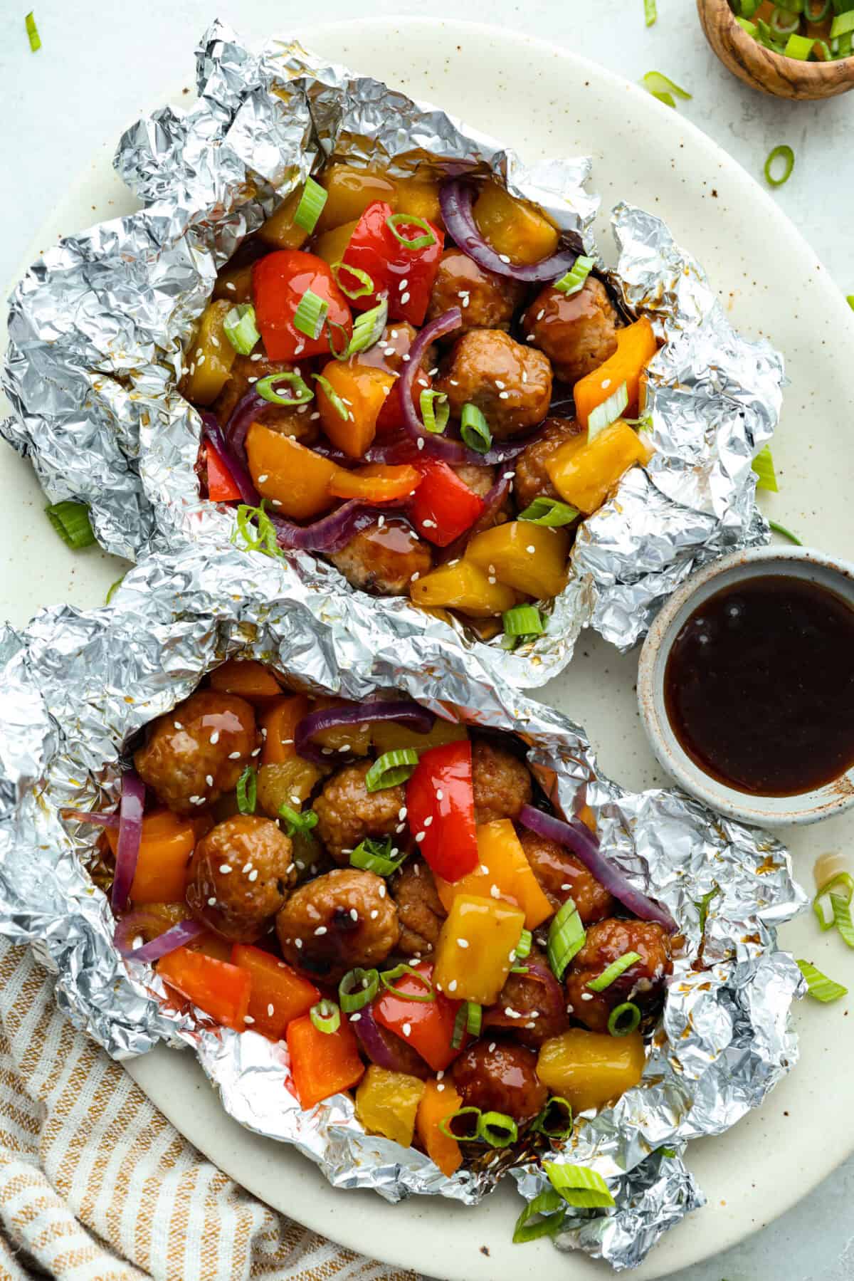 These meatball foil packets have juicy meatballs, sweet pineapple, colorful veggies, covered in sticky teriyaki sauce, and grilled to perfection. Easy to make, fun to eat, and no dishes to wash! Yes, please! Overhead shot of plated teriyaki meatball foil packets.