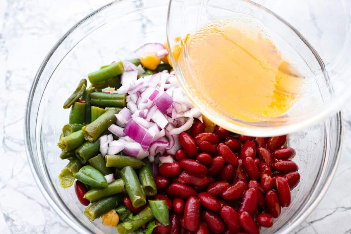 Someone pouring dressing over the top of the three bean salad. 
