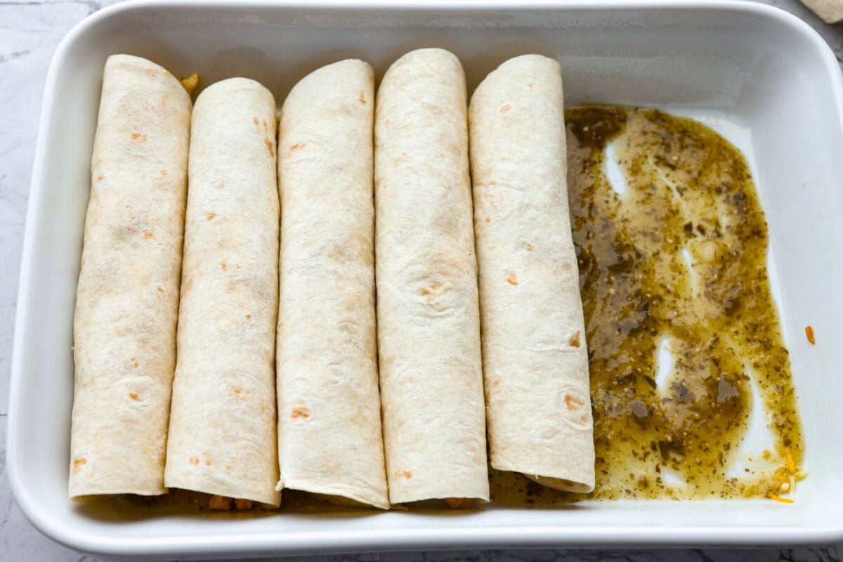 Rolled enchiladas in a pan with salsa verde on the bottom. 