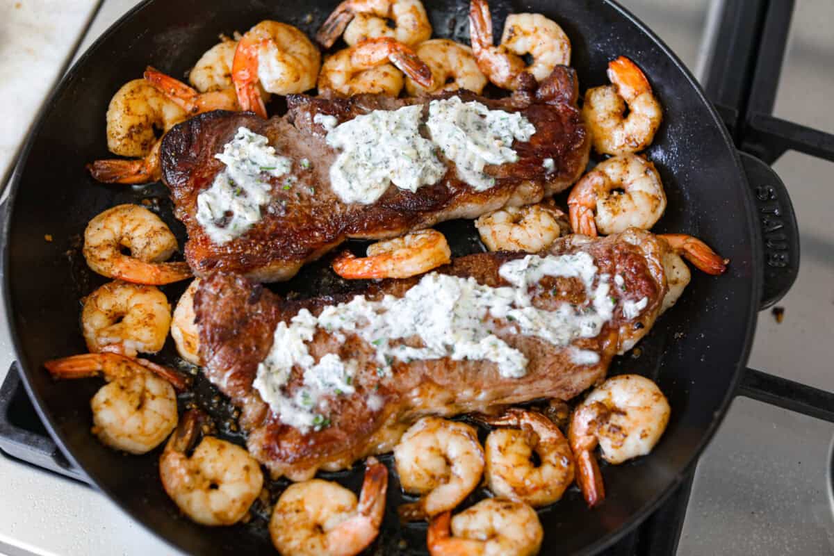Steak and shrimp in the skillet with compound butter added to them. 