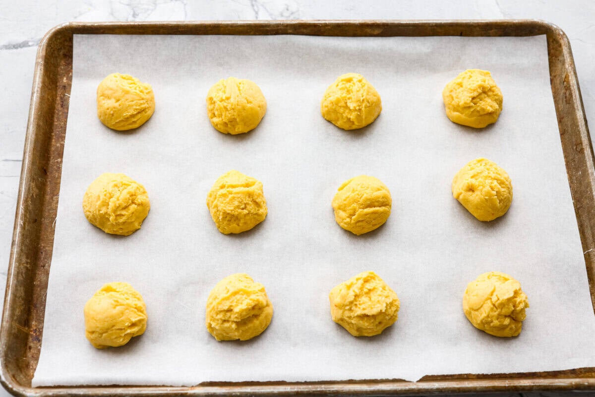 Scoops of cookie dough spread out in parchment paper on a cookie sheet. 