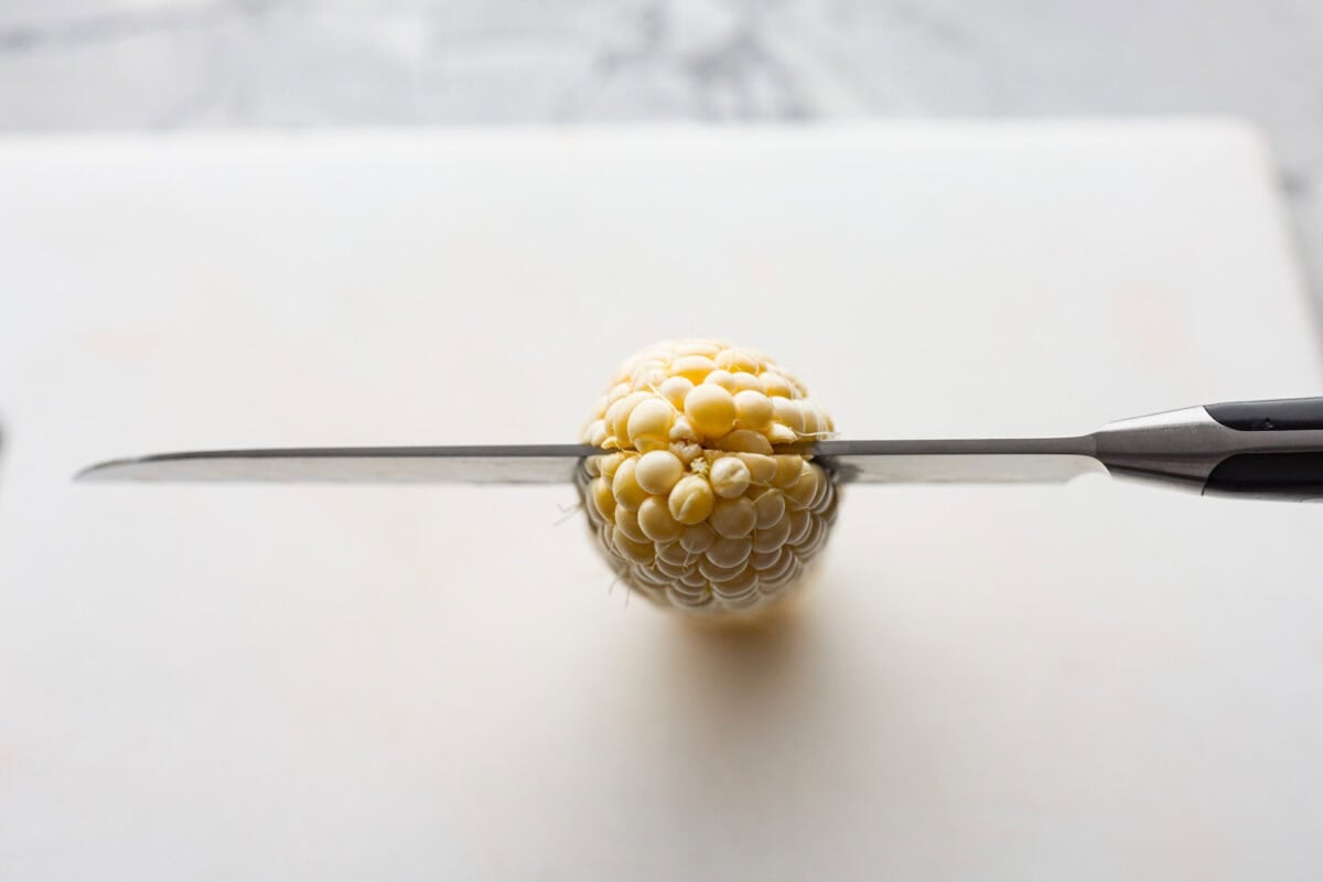 Overhead shot of a knife slicing through the top end of the cob. 