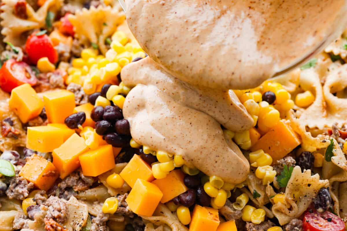 Yeehaw! My cowboy pasta salad is loaded with beef, bacon, beans, and all the fixings for all you cowboy lovers. You'll get all the flavors of the Wild West tossed in the tastiest cowboy salad dressing. Someone pouring the dressing over the salad ingredients.