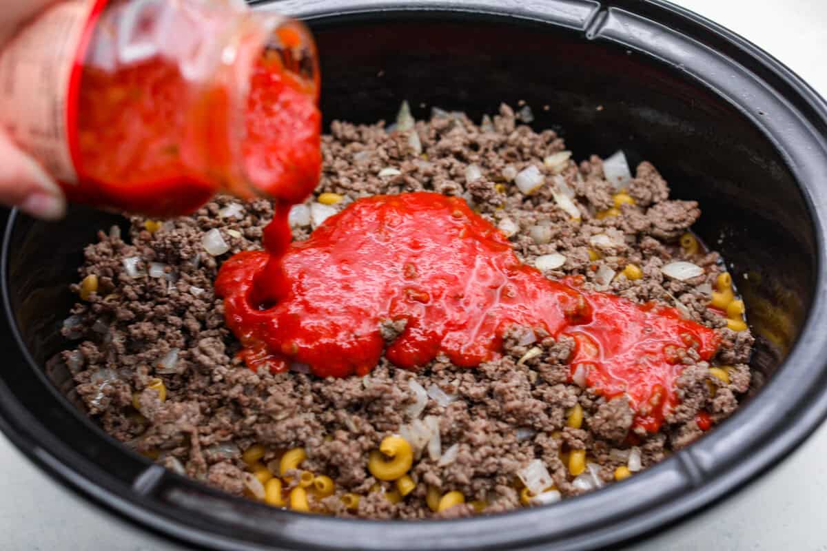 Did you hear back from anyone from thirst? Someone pouring a jar of pasta sauce on top of the ground beef and onion mixture.