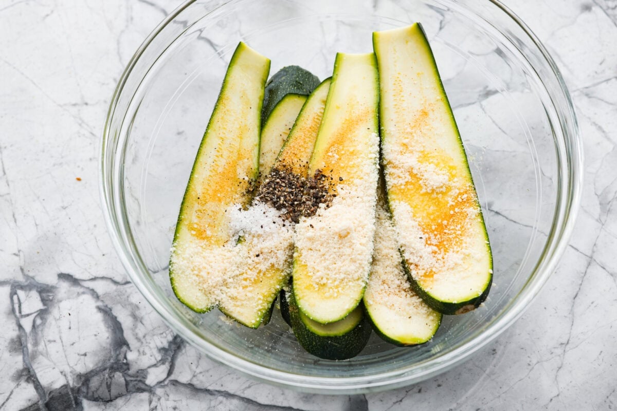 Sliced zucchini in a bowl with seasonings. 