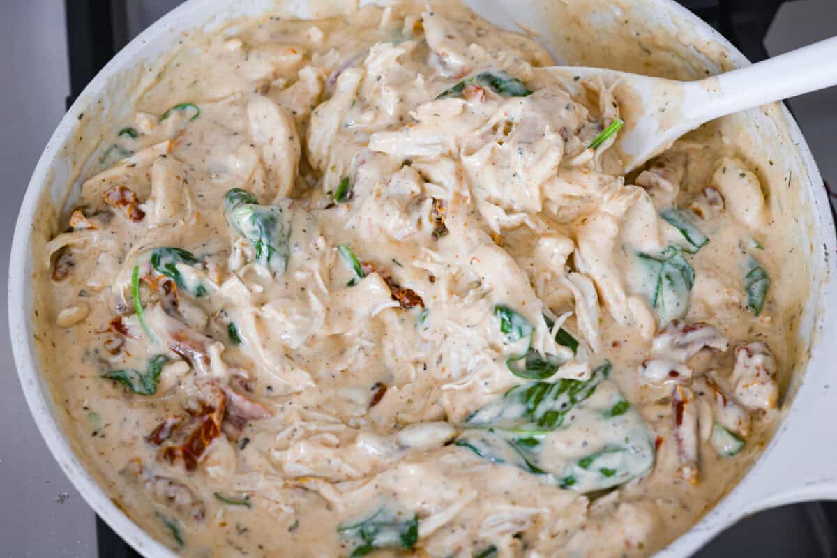 They don’t call it Marry Me Lasagna for nothing! One bite of the creamy sauce, tender chicken, and melty cheese, and everyone will be saying, "YES!" Someone stirring the chicken and spinach into the sauce.