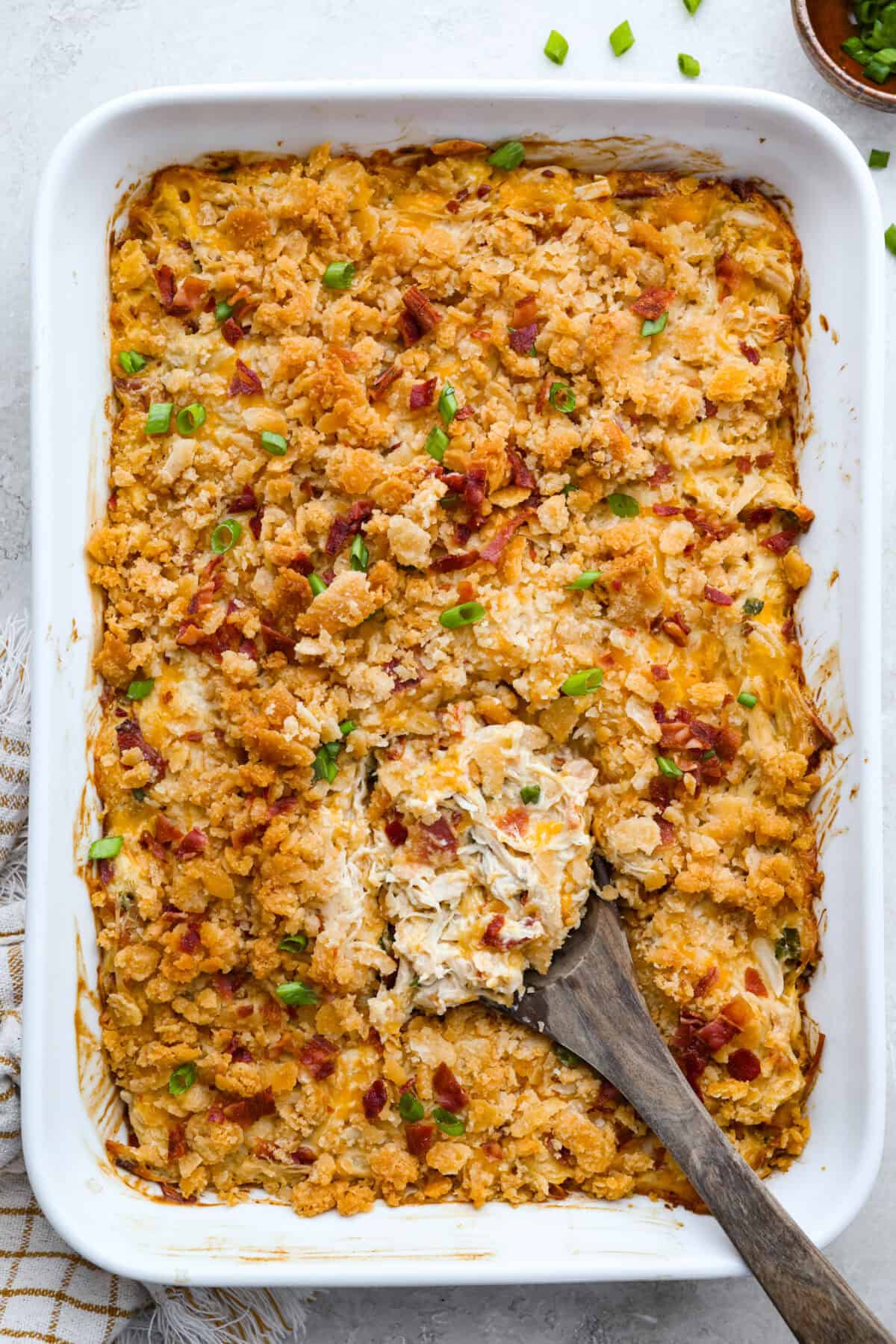Neiman Marcus Chicken Casserole is boujee on a budget. It’s creamy, comforting, and topped with a buttery, golden cracker crust. Inspired by a recipe from the iconic department store’s café, this casserole tastes amazing and comes together fast. Overhead shot of a baked Neiman Marcus chicken casserole with a wooden spoon in it.