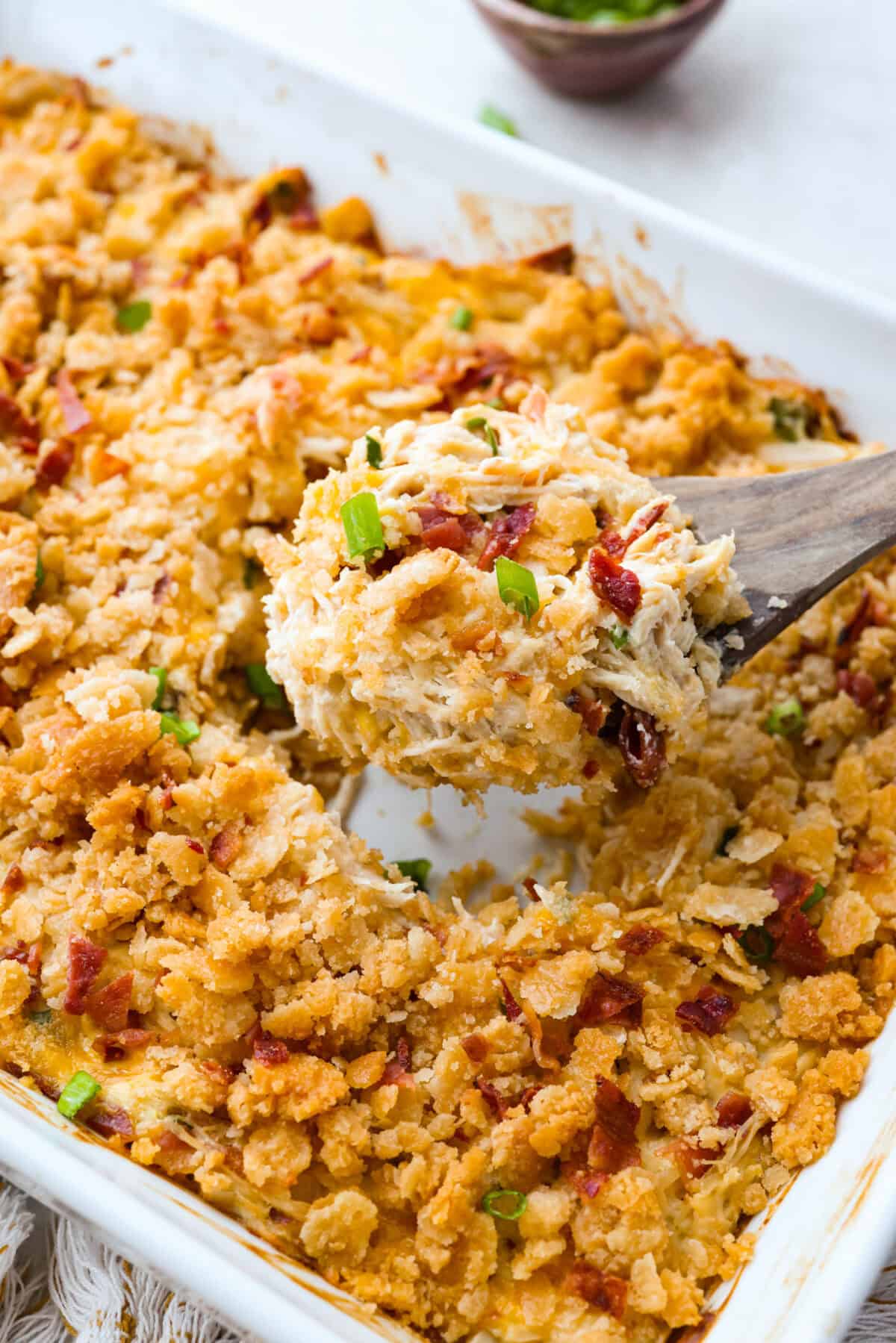 Neiman Marcus Chicken Casserole is boujee on a budget. It’s creamy, comforting, and topped with a buttery, golden cracker crust. Inspired by a recipe from the iconic department store’s café, this casserole tastes amazing and comes together fast. Someone taking a scoop out of the Neiman Marcus chicken casserole dish.