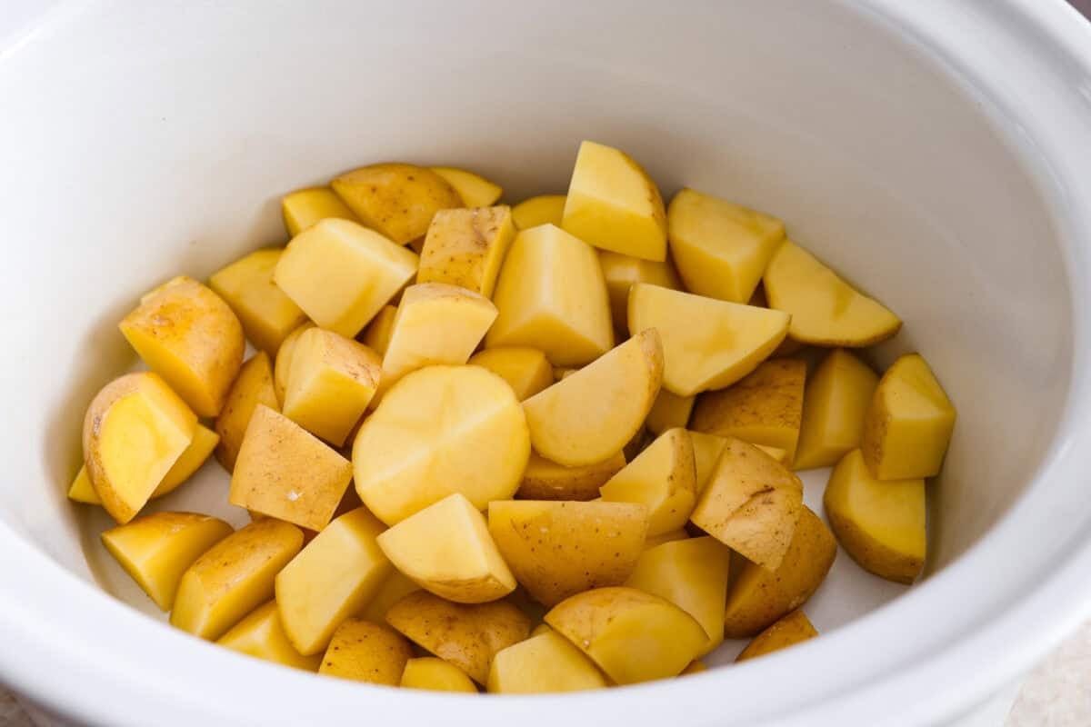 This viral slow cooker Parmesan garlic chicken has juicy meat, tender potatoes, and a sauce so rich and creamy that scooping it with a spoon won’t cut it. You’ll want to drink it, or let’s be real, bathe in it. Potatoes sliced and placed in the bottom of the slow cooker.