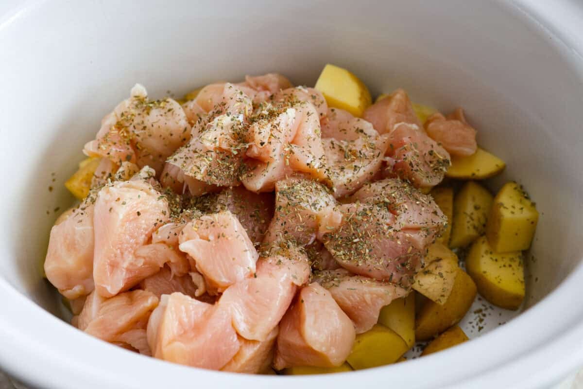 This viral slow cooker Parmesan garlic chicken has juicy meat, tender potatoes, and a sauce so rich and creamy that scooping it with a spoon won’t cut it. You’ll want to drink it, or let’s be real, bathe in it. Cubed chicken with Italian seasoning placed on top of the potatoes in the slow cooker.