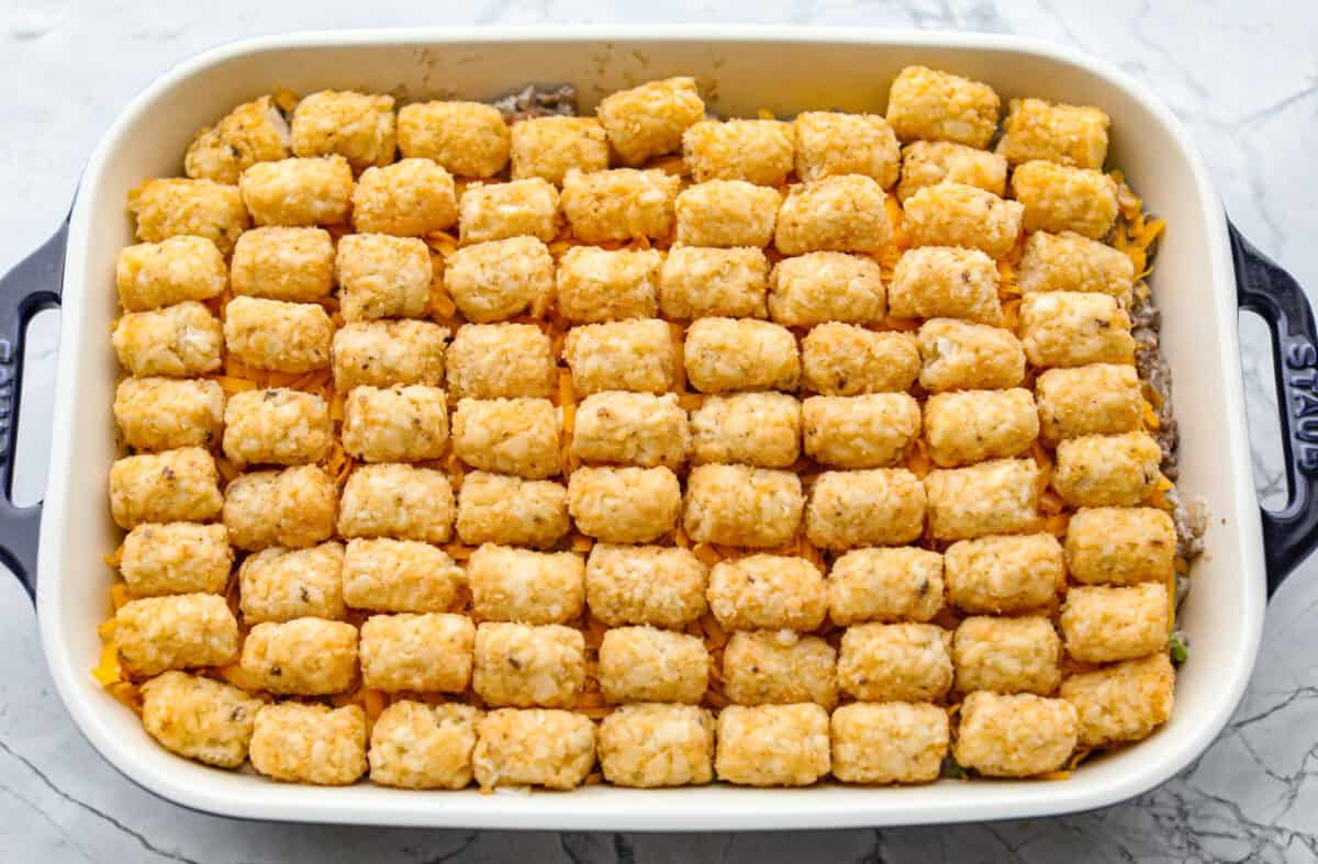 If you love shepherd’s pie, you’ve got to try this Tater Tot Casserole! It’s the ultimate lazy-girl version, with tots instead of mashed potatoes, melty cheese, hearty beef, and total comfort in every bite. The kids will absolutely devour it. Tater tots placed on top of the layered casserole.