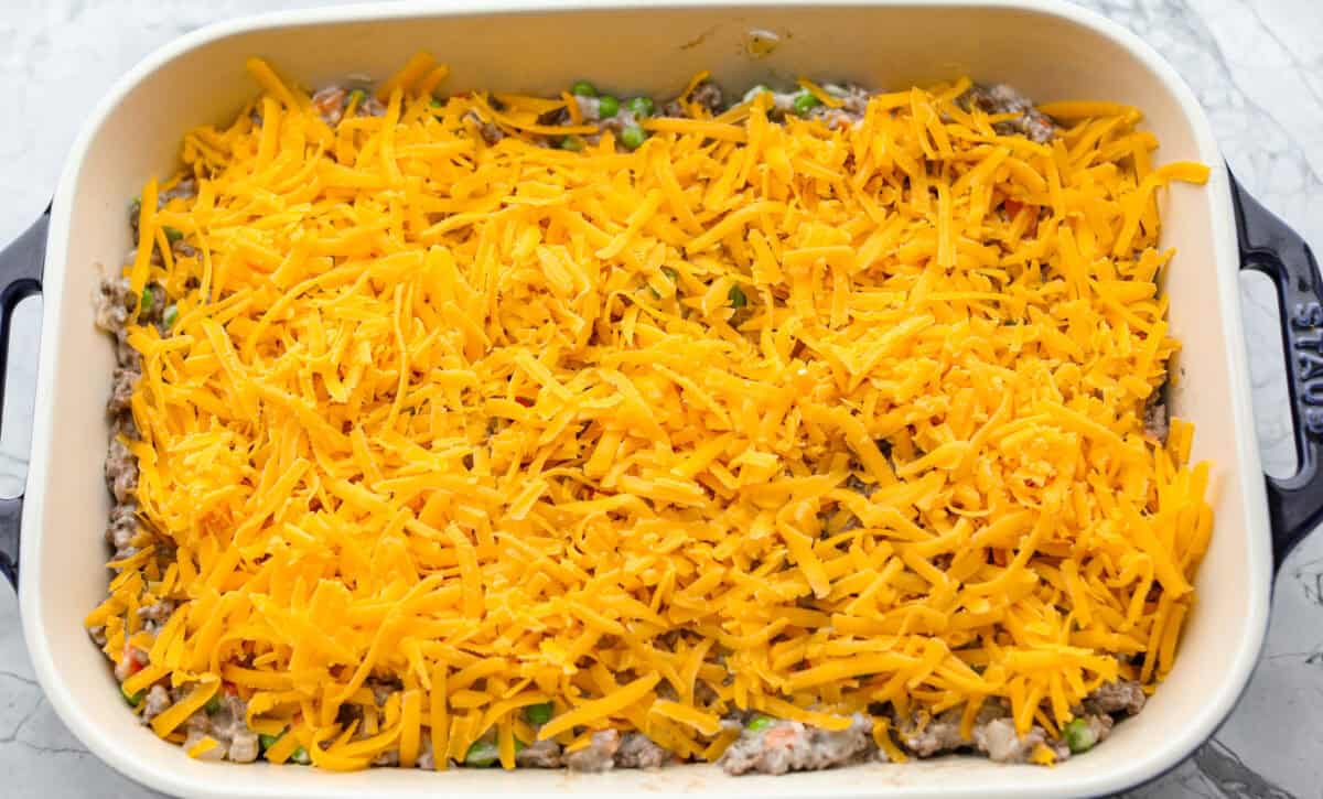 If you love shepherd’s pie, you’ve got to try this Tater Tot Casserole! It’s the ultimate lazy-girl version, with tots instead of mashed potatoes, melty cheese, hearty beef, and total comfort in every bite. The kids will absolutely devour it. Casserole ingredients layered in a baking dish.