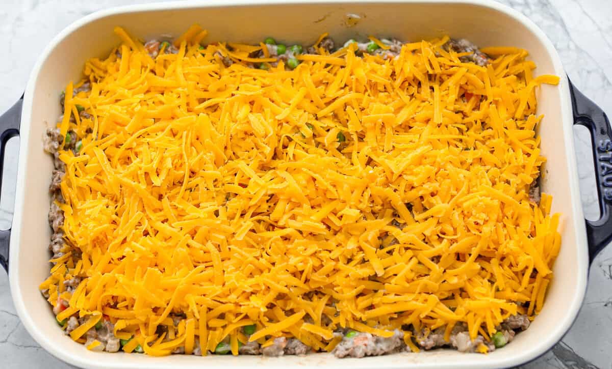 If you love shepherd’s pie, you’ve got to try this Tater Tot Casserole! It’s the ultimate lazy-girl version, with tots instead of mashed potatoes, melty cheese, hearty beef, and total comfort in every bite. The kids will absolutely devour it. Casserole ingredients layered in a baking dish.
