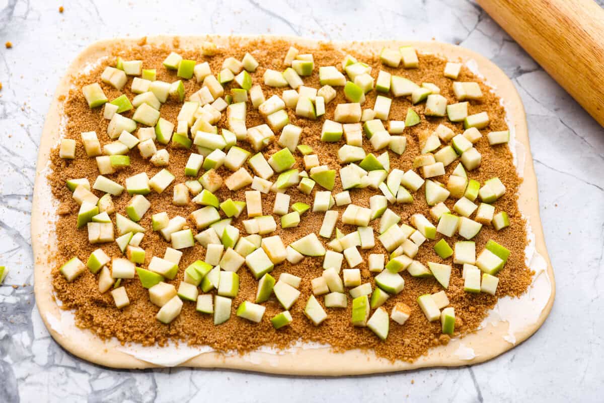 These Caramel Apple Cinnamon Rolls are soft, gooey, and baked with cozy fall flavor in every bite. The homemade dough bakes up perfectly fluffy, and the rich caramel topping makes them feel extra special. Cinnamon sugar mixture and apple slices spread over the butter on the dough.