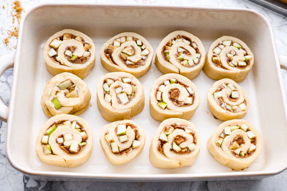 These Caramel Apple Cinnamon Rolls are soft, gooey, and baked with cozy fall flavor in every bite. The homemade dough bakes up perfectly fluffy, and the rich caramel topping makes them feel extra special. Caramel apple cinnamon rolls sliced, placed in a pan, and read to rise.