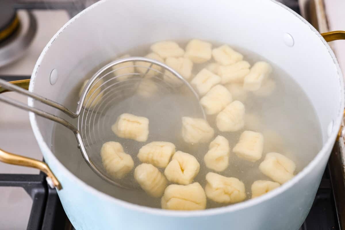 Pot of water with cooked gnocchi pieces. 