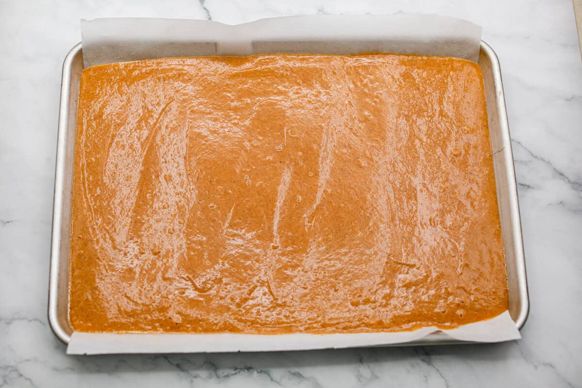 This really is the world’s best pumpkin roll! Soft, moist pumpkin cake wrapped around a sweet cream cheese filling and finished with a dusting of powdered sugar, it’s pure fall magic. The best part? It’s surprisingly easy to make. Cake batter spread out on the parchment paper on a jelly roll pan.