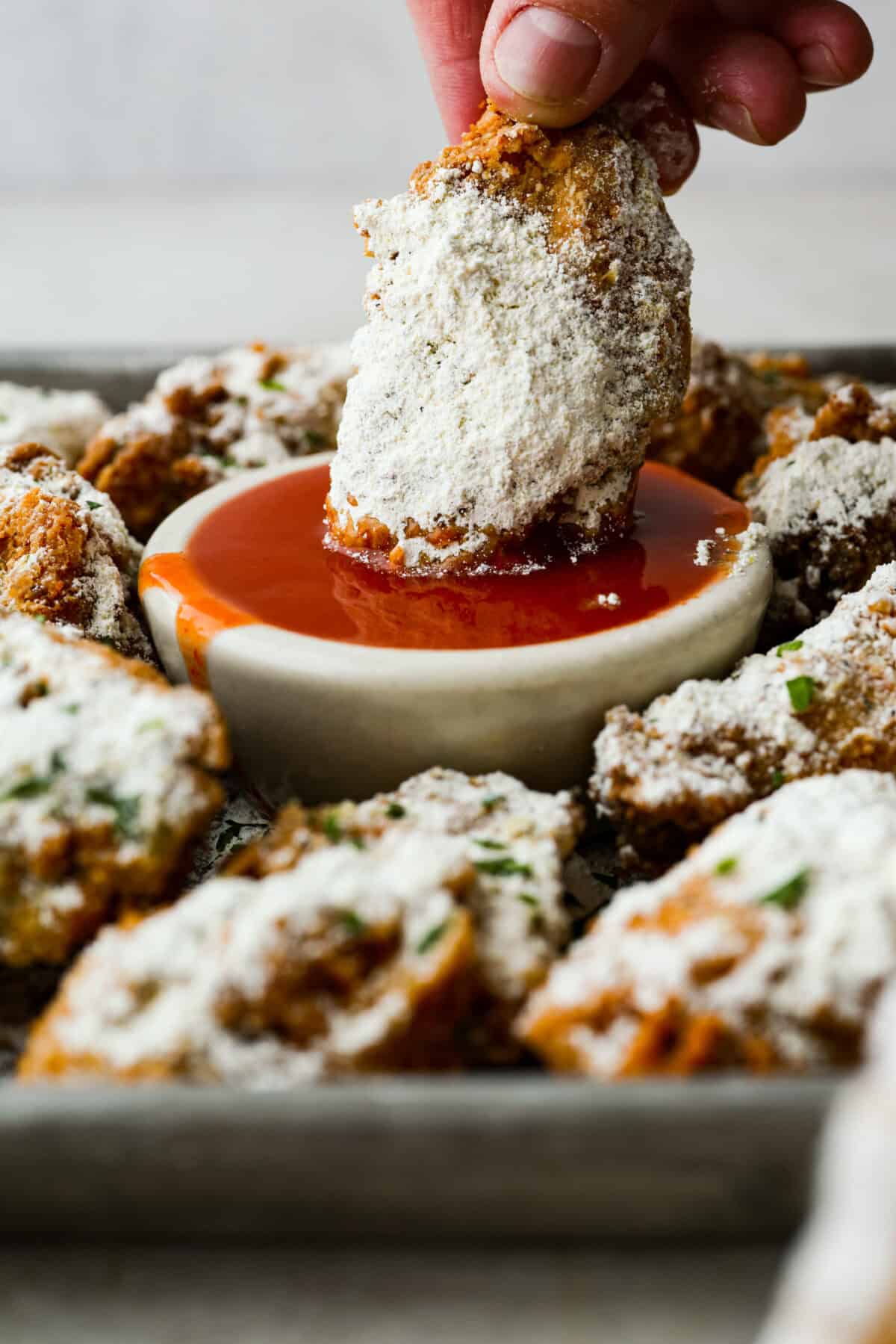 Meet your new wing obsession: Crack Wings. Salty, tangy, peppery, with a touch of sweetness. I've never seen a wing with a powder dusting so full of flavor! They are addictive because of the salty and sweet combo with that hint of heat. Someone dipping a crack wing into a small bowl of hot sauce.