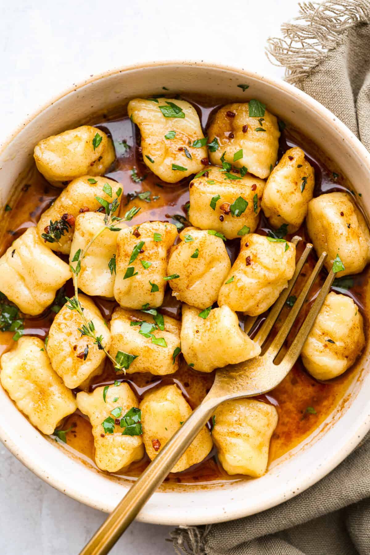Bowl of cooked homemade potato gnocchi in a bowl with brown butter and herbs.