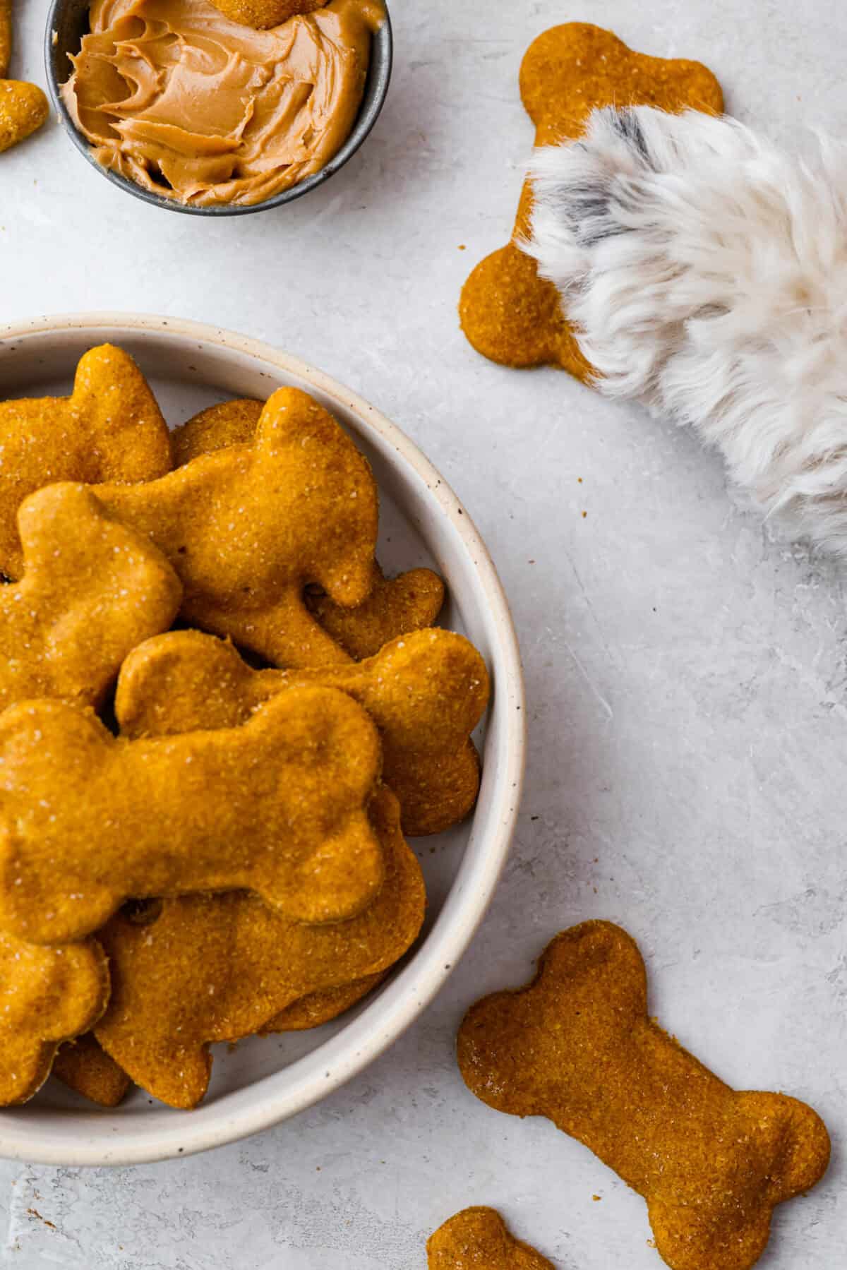 Bowl of homemade dog treats next to a dog paw on a dog treat.