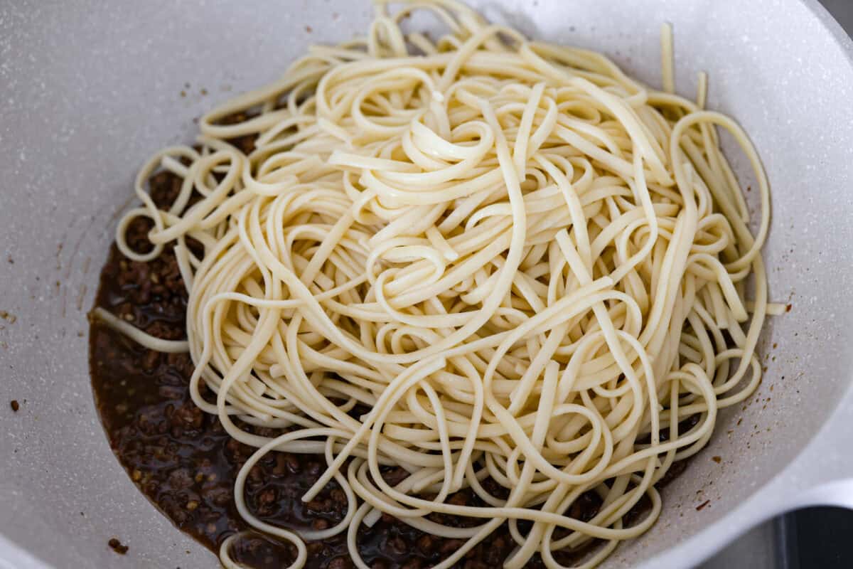 Noodles being added to the sauce and beef mixture.