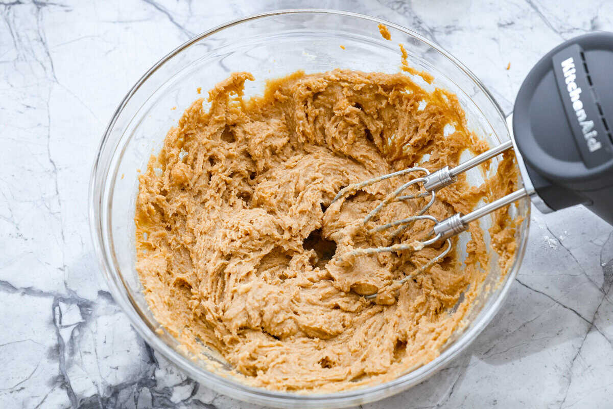 If you grew up in Utah, Lunch Lady Peanut Butter Bars were basically a rite of passage. Thick, chewy, and slathered in chocolate frosting. My version is even better, and yes, this one earned its spot in my cookbook for a reason. Someone mixing butter, brown sugar, and peanut butter in a bowl with a hand mixer.