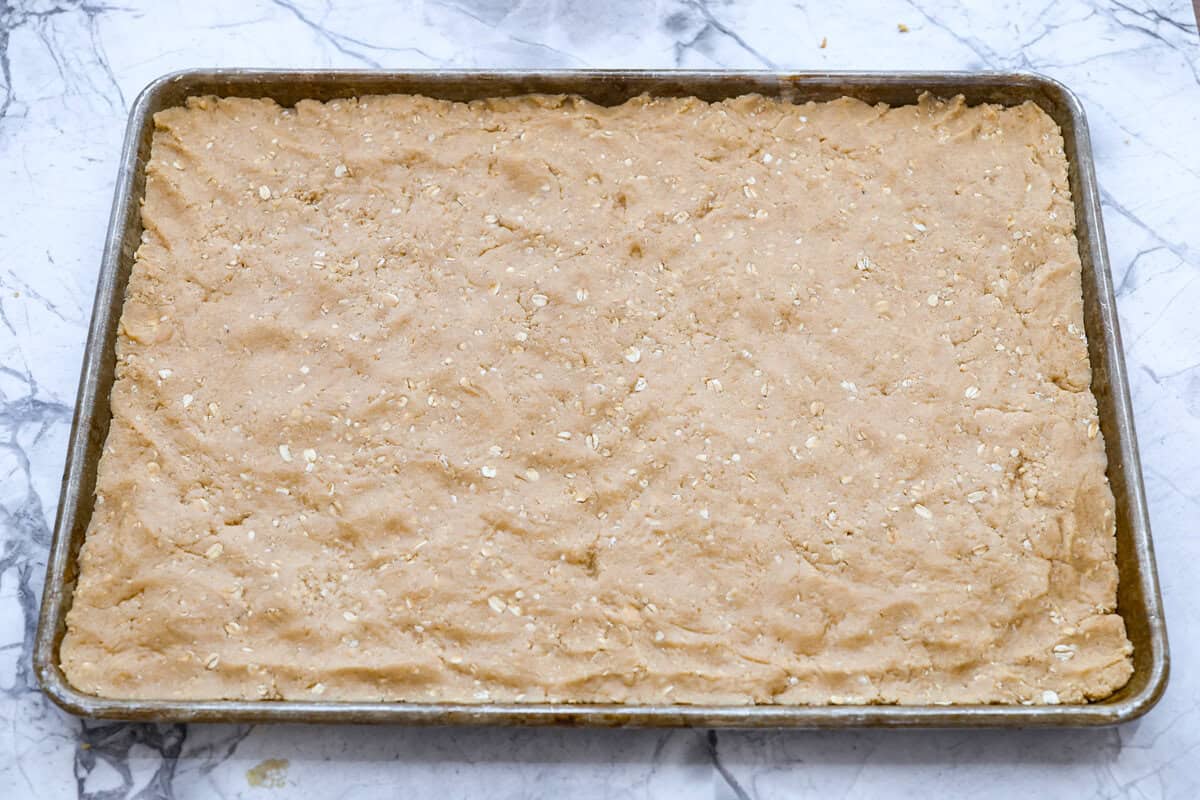 If you grew up in Utah, Lunch Lady Peanut Butter Bars were basically a rite of passage. Thick, chewy, and slathered in chocolate frosting. My version is even better, and yes, this one earned its spot in my cookbook for a reason. Bar batter smashed and spread out into a cookie sheet.