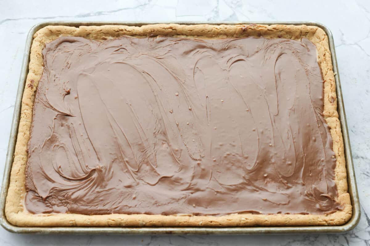 Chocolate frosting spread out on top of the peanut butter layer on the peanut butter bars. 