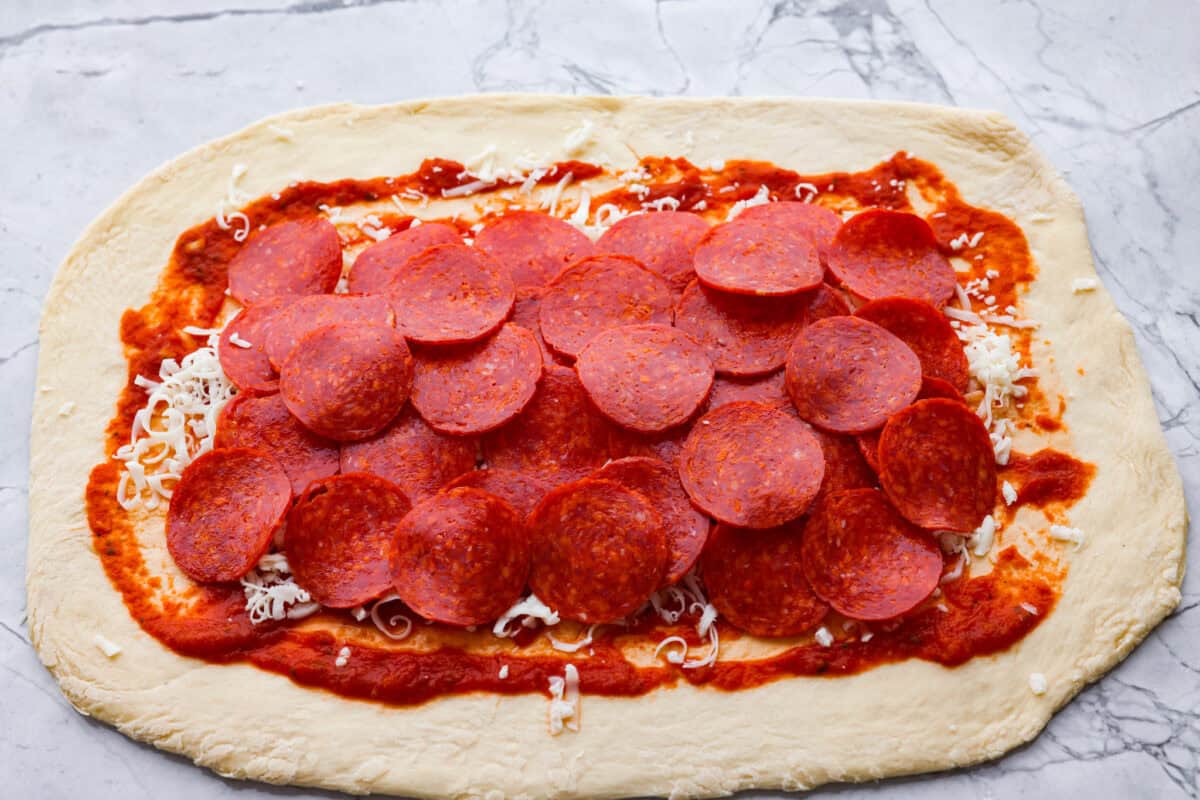 Sauce, cheese and pepperoni's spread out on the pizza dough. 