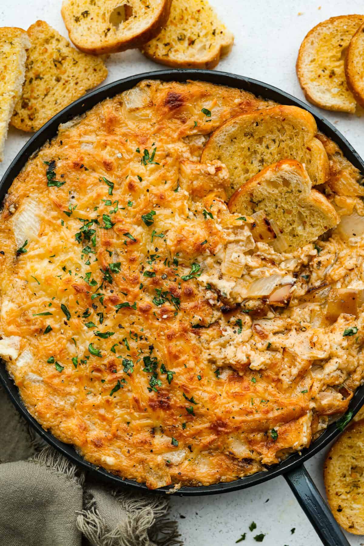 My Tennessee Onion Dip is a family-party legend. Everyone always begs me to bring it, and for good reason, the sweet onion flavor baked with gooey cheese and seasonings is absolutely irresistible! Skillet full of Tennessee onion dip, with a few slices of crostini.