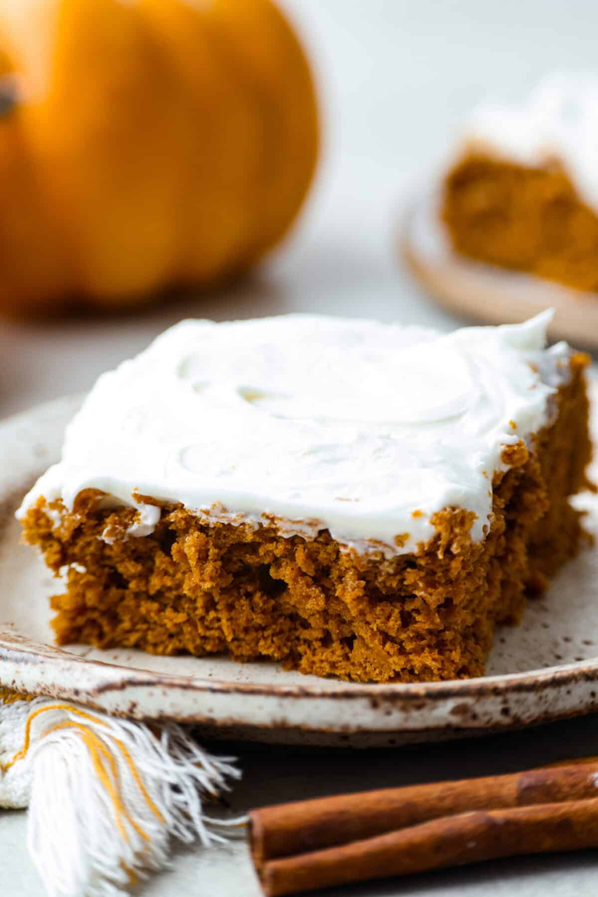 This 2 ingredient pumpkin cake comes together in minutes and bakes up perfectly spiced, tender, and fluffy every single time. It’s the ultimate dessert for any fall gathering or when the sweet tooth hits! Slice of 2 ingredient pumpkin cake on a plate with cinnamon sticks in the foreground and a pumpkin in the background.