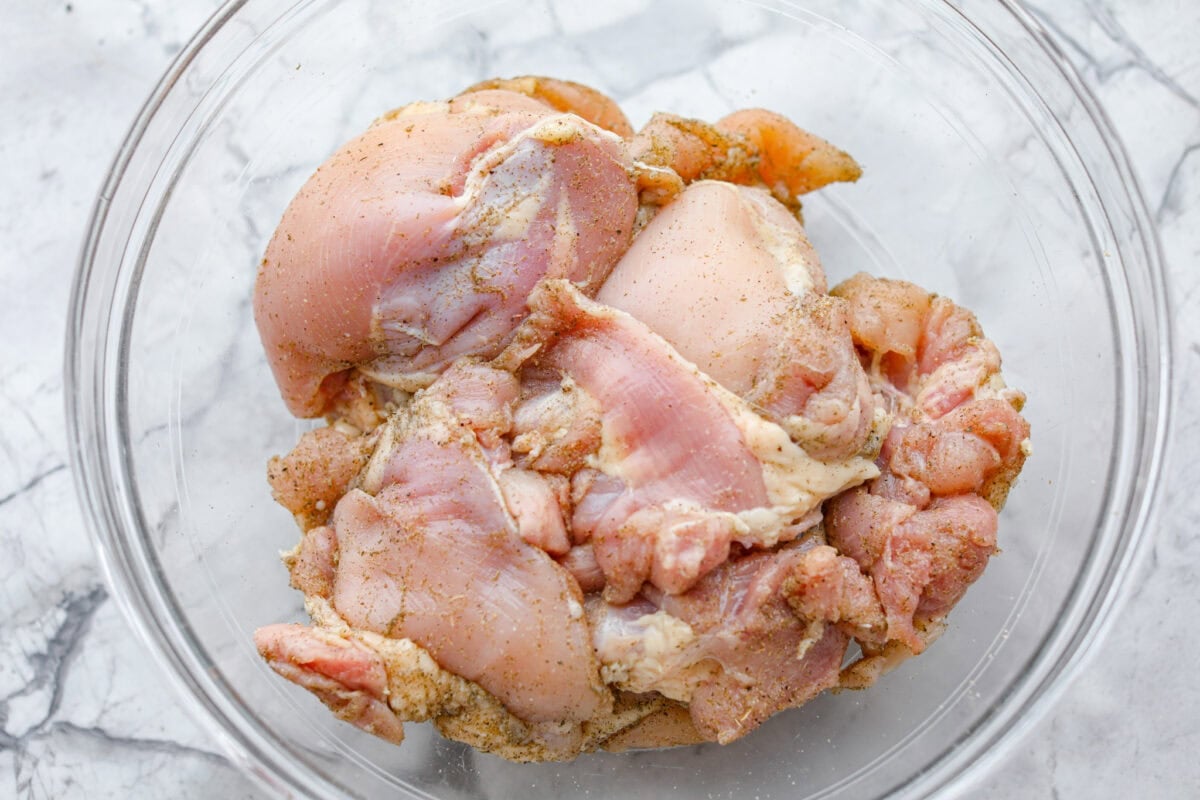 Apple cider chicken thighs bring all the best fall flavors to your plate! Juicy chicken, caramelized apples, and a rich cider sauce for the ultimate cozy dinner. Chicken thighs coated with seasonings sitting in bowl.