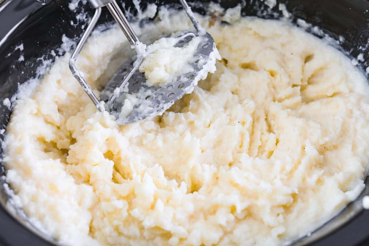 Someone mashing the potatoes in the crockpot.