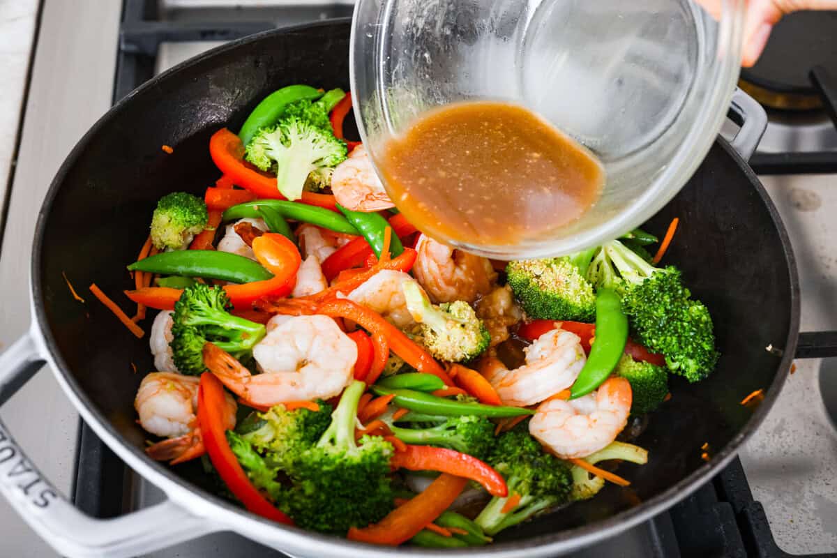 Some nights you just need dinner on the table fast! That’s when this garlic shrimp stir fry saves the day. Juicy shrimp, crisp veggies, and the BEST garlicky sauce all come together in 20 minutes. Garlic sauce poured over shrimp and veggies in the wok.