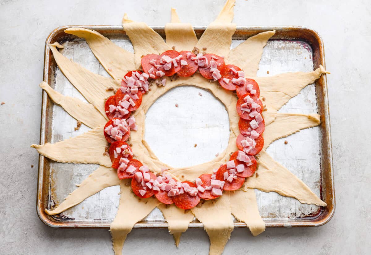 Pizza night just got a glow-up! This fun pull-apart pizza ring is perfect for family dinner, game day, or a party snack. Easy to make, endlessly customizable, and totally kid-approved, you’ll be reaching for slice after slice! sauce and toppings in a ring on the sunburst crescent dough shape.