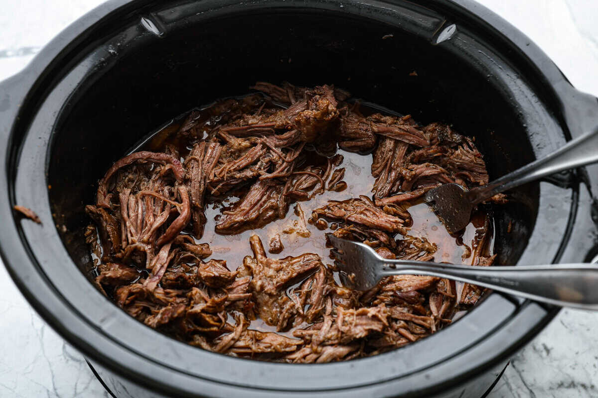 Slow cooker barbacoa beef simmers all day in smoky chipotle, tangy lime, and warm spices until it falls apart. It’s perfect for tacos, burritos, bowls, or nachos, all with that taquería-style flavor at home. Someone breaking apart the beef with forks in the slow cooker.