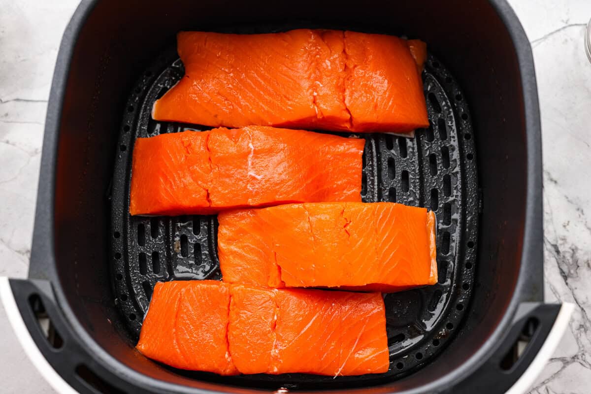 Air fryer teriyaki salmon is the best fast and tasty meal! The salmon cooks up perfectly tender with crisp edges, then gets coated in a glossy, sweet-and-savory teriyaki glaze that I know you'll love! Salmon fillets skin side down in the bottom of the air fryer basket.