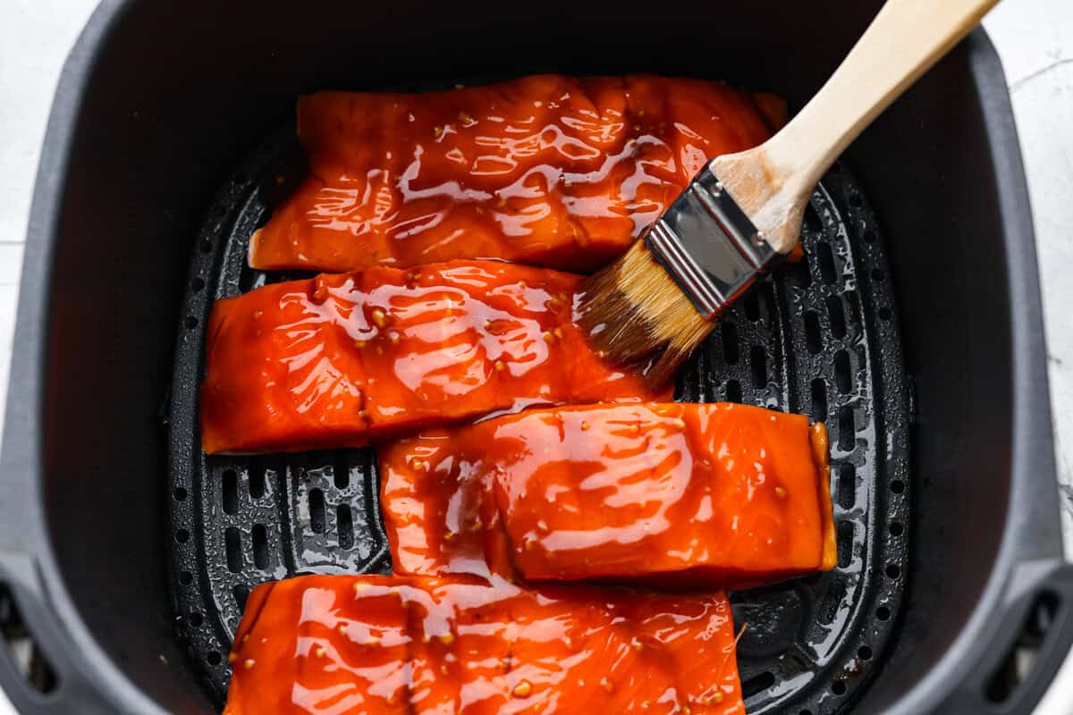 Air fryer teriyaki salmon is the best fast and tasty meal! The salmon cooks up perfectly tender with crisp edges, then gets coated in a glossy, sweet-and-savory teriyaki glaze that I know you'll love! Someone brushing the teriyaki glaze on the salmon.