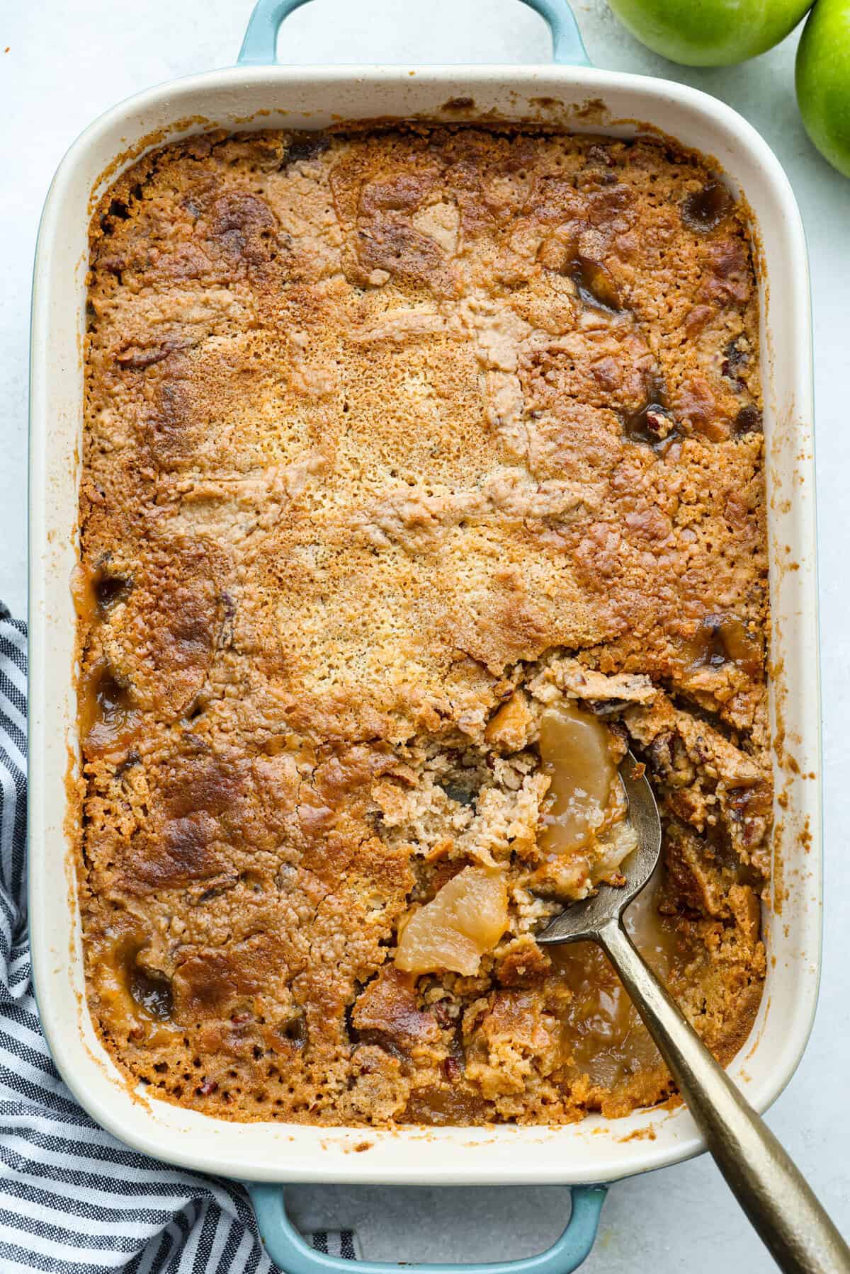 This Apple Dump Cake is your new dessert BFF. You can just toss it together, pop it in the oven, and let the magic happen. Sweet, simple, and seriously so delicious. Overhead shot of apple dump cake mix in a baking dish and a serving spoon.