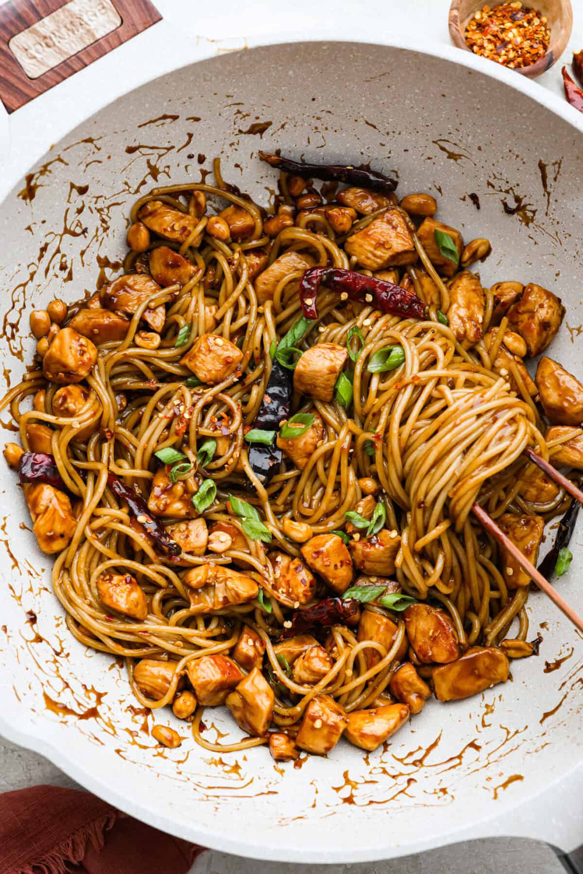 Skip the takeout, these Kung Pao Chicken Noodles are spicy, saucy, and loaded with flavor! Tender chicken, chewy noodles, crunchy peanuts, and a kick of heat all come together in one quick and easy dish that’s perfect for weeknight dinners. Overhead shot of someone tossing the sauce in with the Kung Pao chicken noodles.