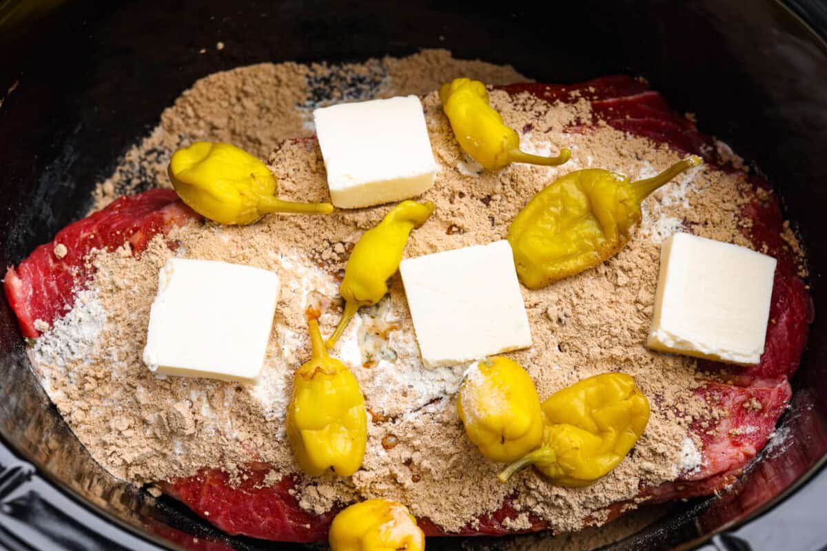 This Mississippi pot roast is melt-in-your-mouth tender, full of rich flavor, and couldn’t be easier. Just five ingredients and your slow cooker does all the work! It's a Sunday favorite at our house, and I know you'll love it too! Chuck roast covered in the seasoning packets, butter, and peppers.