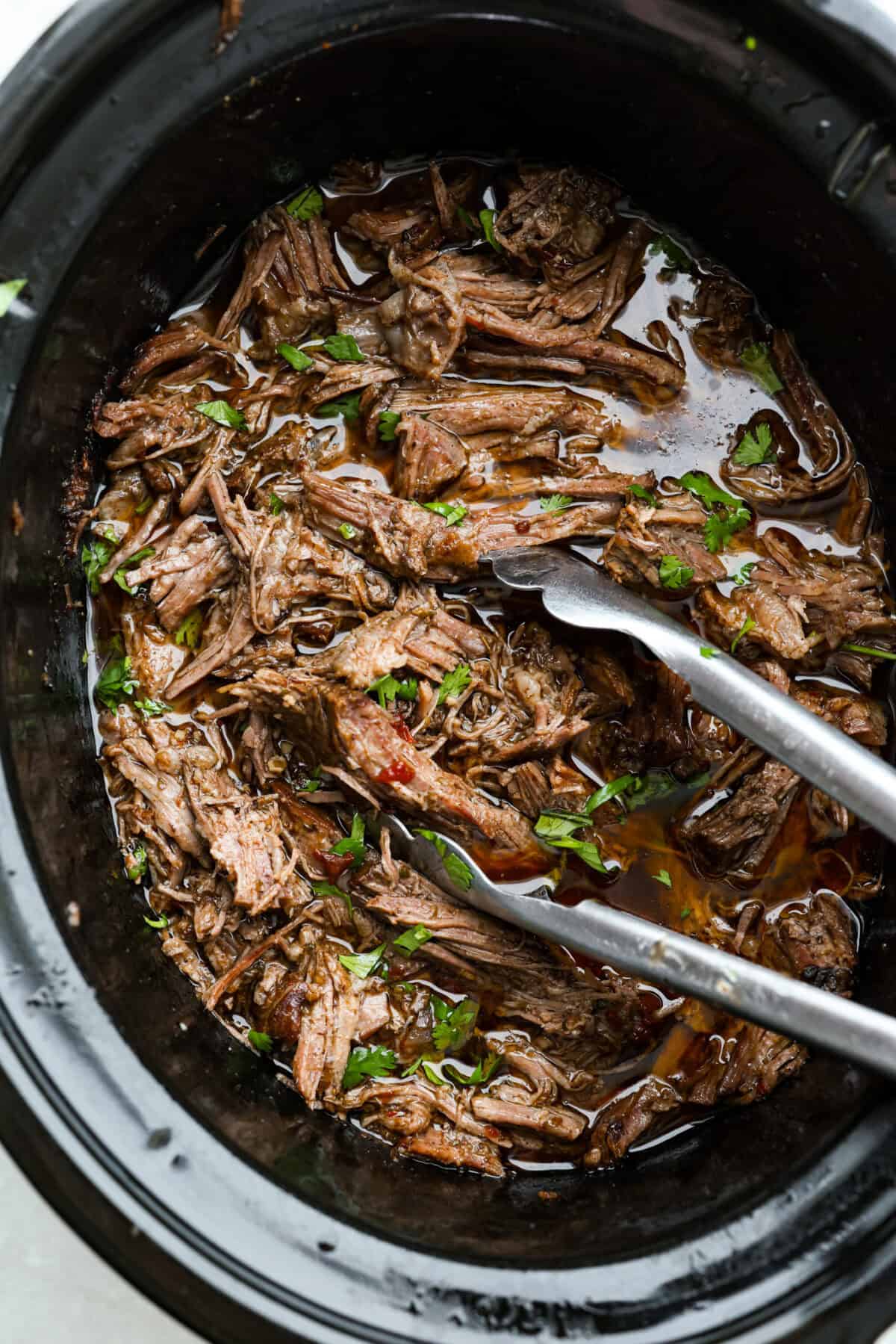 Slow cooker barbacoa beef simmers all day in smoky chipotle, tangy lime, and warm spices until it falls apart. It’s perfect for tacos, burritos, bowls, or nachos, all with that taquería-style flavor at home. Overhead shot of slow cooker Barbacoa beef still in the crockpot.