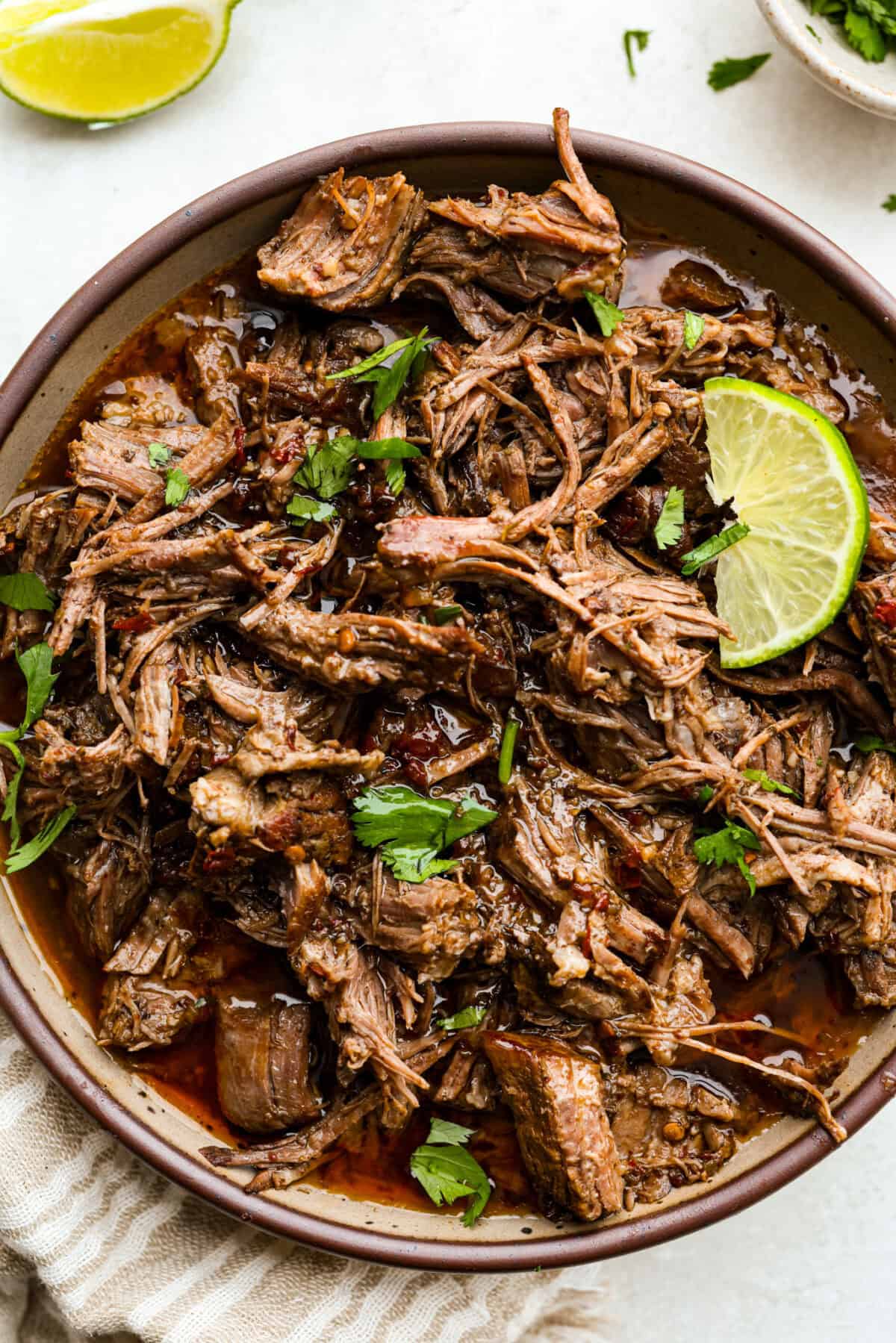Slow cooker barbacoa beef simmers all day in smoky chipotle, tangy lime, and warm spices until it falls apart. It’s perfect for tacos, burritos, bowls, or nachos, all with that taquería-style flavor at home. Bowl of slow cooker Barbacoa beef garnished with cilantro and lime.