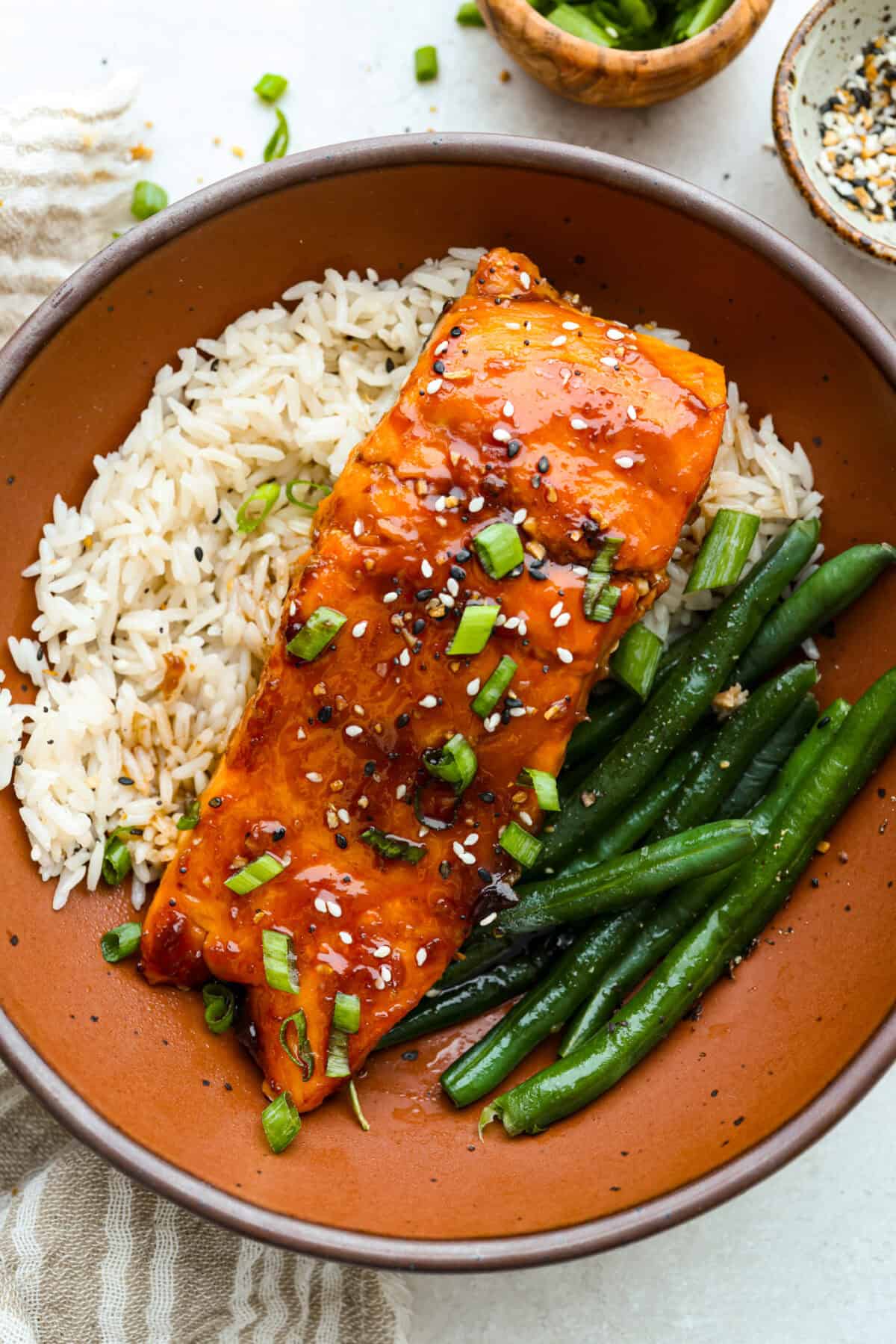 Plated air fryer teriyaki salmon filet on a bed of white rice and a side of green beans. 