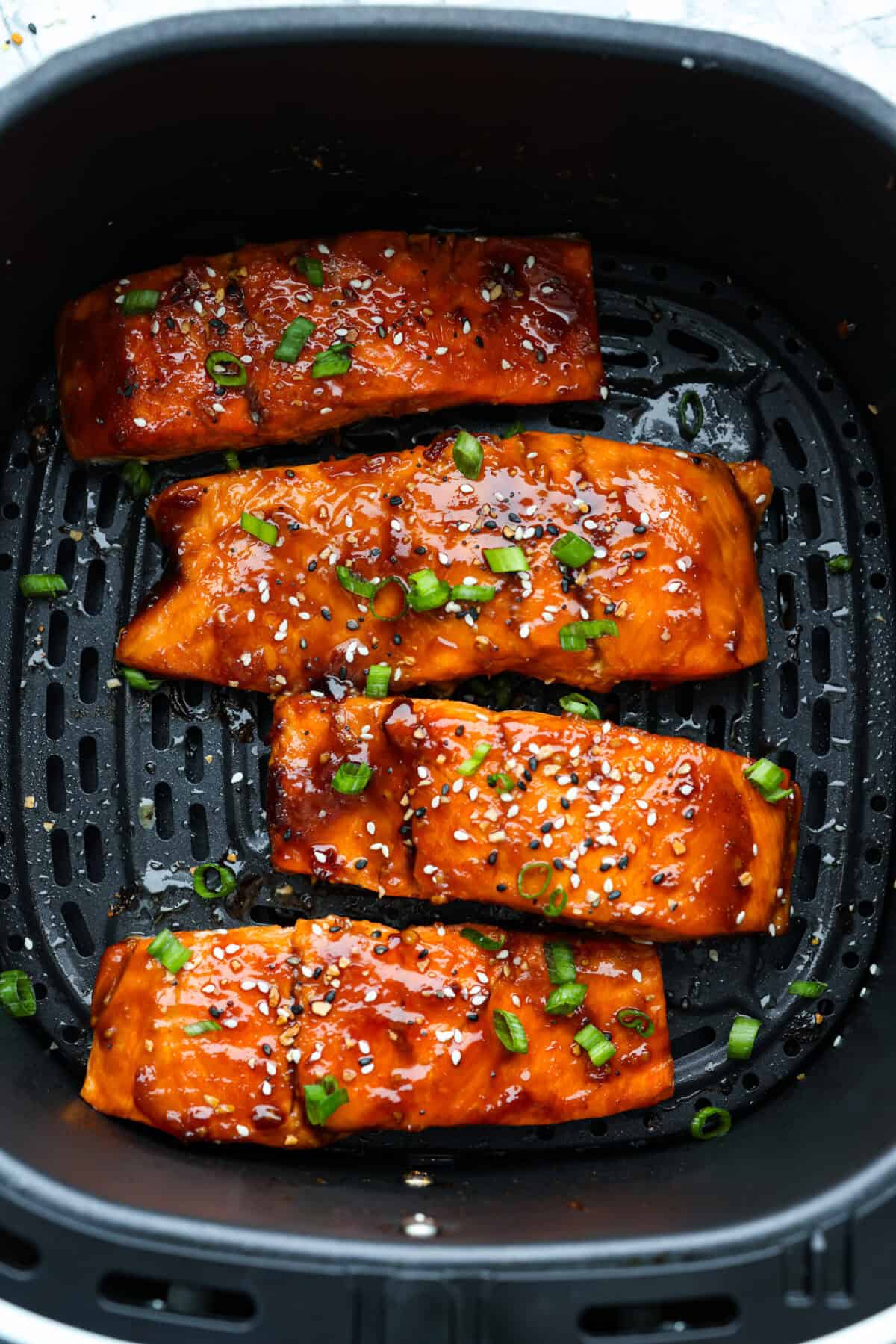 Cooked air fryer teriyaki glazed salmon garnished with black and white sesame seeds and chopped green onion.